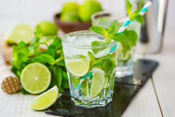 Two fresh mojitos cocktail in glass on wooden table. Mojitos with mint leaves, lime and ice. Drink making tools and ingredients for cocktail. 