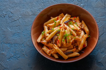 Close up of italian penne pasta with eggplants and tomato sauce in a brown bowl on a black stone background. Copy space and overhead view. Traditional food concept.