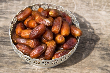 Dates fruit on a silver bowl on wooden table. The Muslim feast of the holy month of Ramadan Kareem