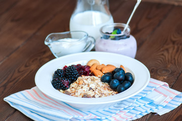 Healthy breakfast concept. Homemade muesli with blackberry, dry cranberry, blueberry, almond, yogurt in a jar, sour cream and milk on a wooden background. Close up and copy space.