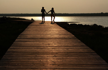 Fototapeta premium Two siblings walking along a boardwalk into the sunset.