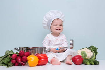 Baby wearing a chef hat with vegetables and pan. .