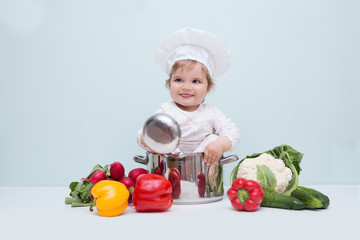 Baby wearing a chef hat with vegetables and pan. .