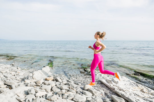 Young attractive fitness girl running on stones beach