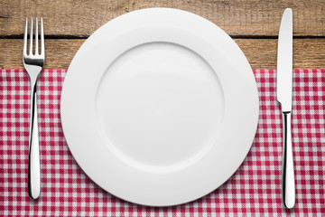 empty plate on a wooden background, a napkin in a red and white cage, a fork a knife