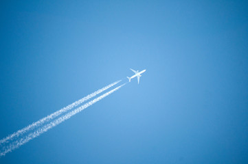 White jet plane flies high in the blue sky and leaves behind a white contrail