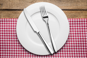 empty plate on a wooden background, a napkin in a red and white cage, a fork a knife