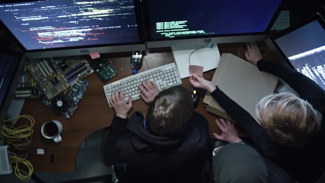 Top view of three hackers working with programming code on computers in dark office