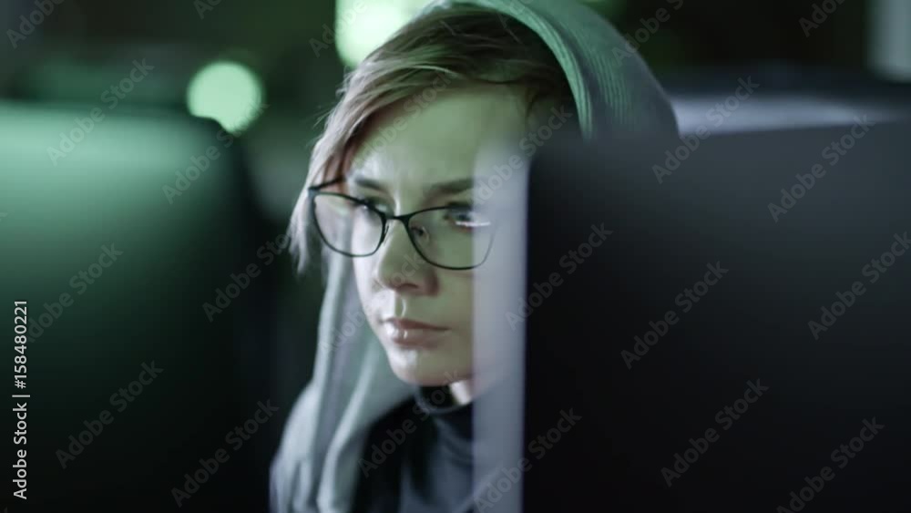 Wall mural closeup shot of young woman in eyeglasses sitting in front of computer and reading programming code