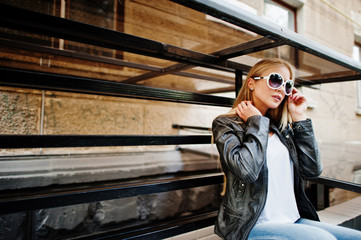 Stylish blonde woman wear at jeans, suglasses, choker and leather jacket at street. Fashion urban model portrait.