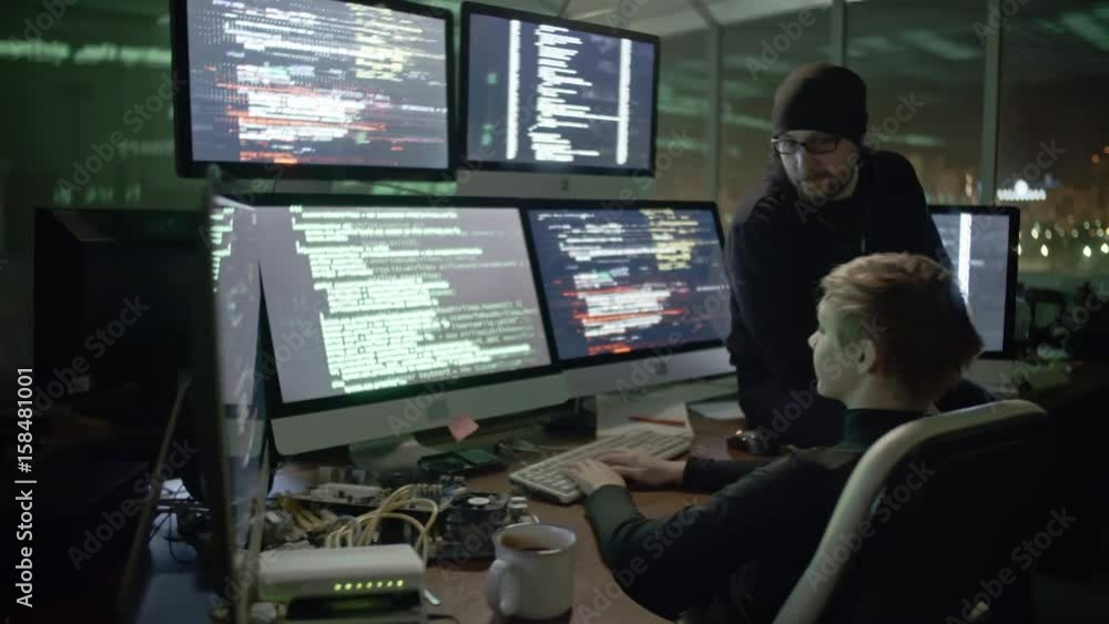 Wall mural young woman typing program codes on computer screens while cracking website with male colleague. man