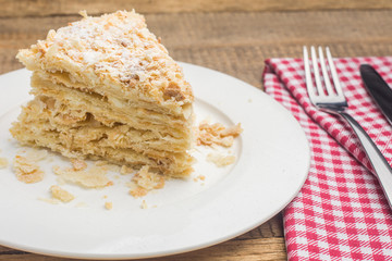 cake Napoleon on a white plate, on a wooden background and a red-white napkin