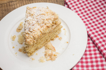cake Napoleon on a white plate, on a wooden background and a red-white napkin