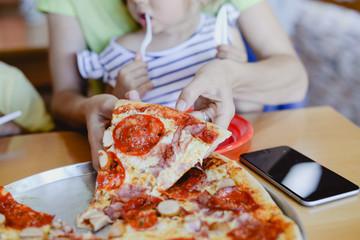 Closeup of people eat and work. Hands, sliced pizza and using smartphone on restaurant table background. Communication, friendship, leisure lifestyle