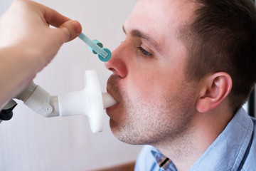 Young man testing breathing function by spirometry. Doctor closing his nose
