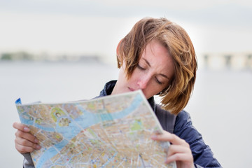 A beautiful girl in a denim jacket is holding a map and trying to understand where she is. Lost in...