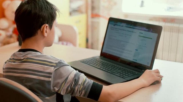 Hard of hearing teenager in hearing aids sitting at table using laptop