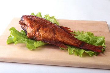Smoked fish and lemon on green lettuce leaves on Wooden cutting board isolated on white background.