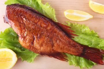 Smoked fish and lemon on green lettuce leaves on Wooden cutting board isolated on white background.