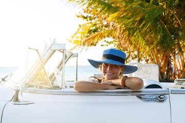 Fototapeta premium Beautiful woman in blue hat and white retro cabriolet