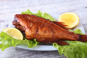 Smoked fish and lemon on green lettuce leaves on Wooden cutting board isolated on white background.