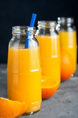 Fresh Orange Juice, Glass Bottle of Juice,Wooden Tray, Straws,Grey Table, Dark Background.