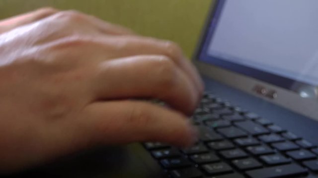 Caucasian man hands printing on laptop keyboard. Closeup view of computer with green wall behind. Office scene. Blurred.