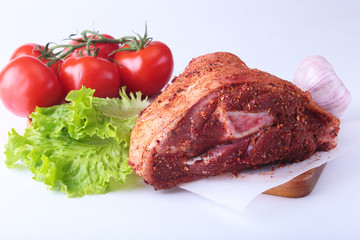 Raw pork knuckle and vegetables, garlic, tomatoes spices and lettuce leaves on a cutting board. Selective focus. Ready for cooking.