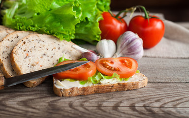 Sliced bread and a sandwich with tomatoes and salad on a wooden table. The concept of breakfast.