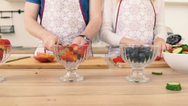 Close-up of the hand of a man and woman who prepare a fruit salad with strawberries.