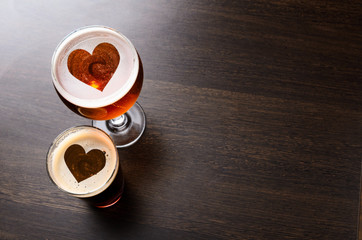 Heart silhouettes in two glasses of fresh beer on pub table, view from above