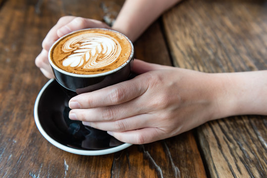 lady's hand holding a cup of coffee with fern shape latte art