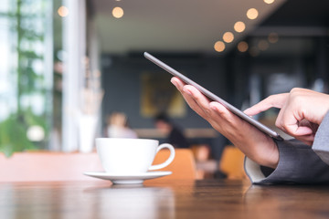A business woman's hands holding and pointing at tablet with coffee cup on wooden table in modern cafe