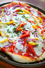 Pizza with salami, onion, red and yellow bell peppers and mozzarella cheese