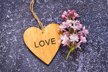 A bunch of lilacs and wooden heart with word love on it on a blue textured cement background