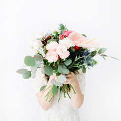 Pretty woman with beautiful flowers bouquet: bombastic roses, blue eringium, anthurium flower, eucalyptus branches at white wall. Front view. Floral lifestyle composition.