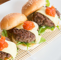 close up of mini burgers with cheese, onion and pickle.