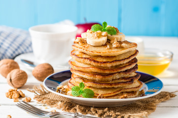 Pancakes with banana, honey, walnuts and mint on plate.