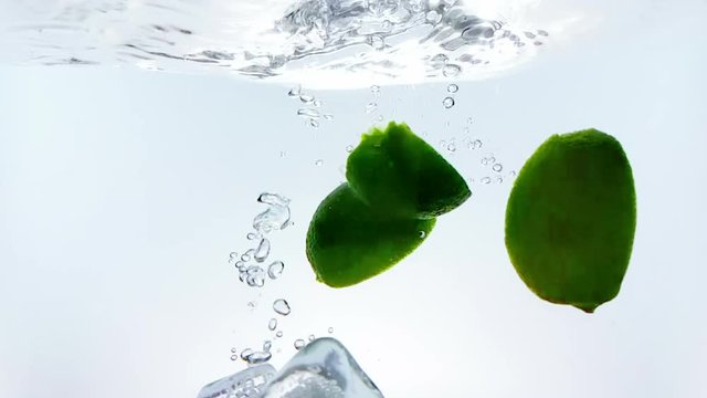 lime fruit and ice cubes splash falling down into white cocktail and water drinking glass, shot in slow motion on white background, fun, nutrition and drink concept