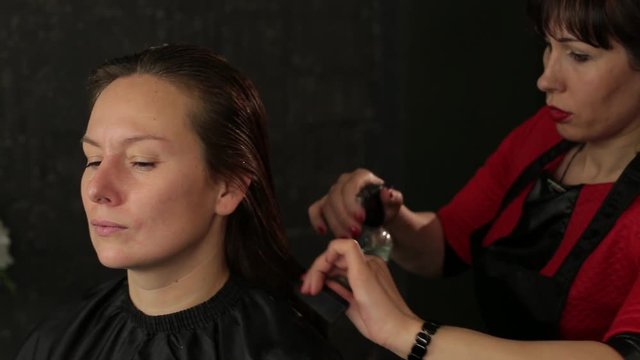 Master hairdresser with a mustach styling hair with spray. Redhead girl