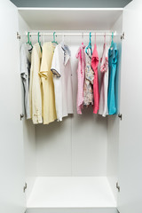 Clothes hanging on rail in white wardrobe. Men's and women's summer clothes, pastel colors