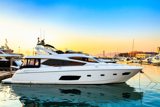 Fototapeta Luxury yacht docked in sea port at sunset. Motor boats and blue water. Relaxation and fashionable vacation.