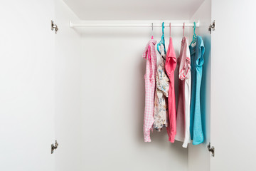 Clothes hanging on rail in white wardrobe. Men's and women's summer clothes, pastel colors