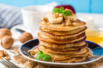 Pancakes with banana, honey, walnuts and mint on plate.