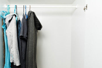 Clothes hanging on rail in white wardrobe. Men's and women's autumn or winter  clothes, grey and dark colors. Copy space