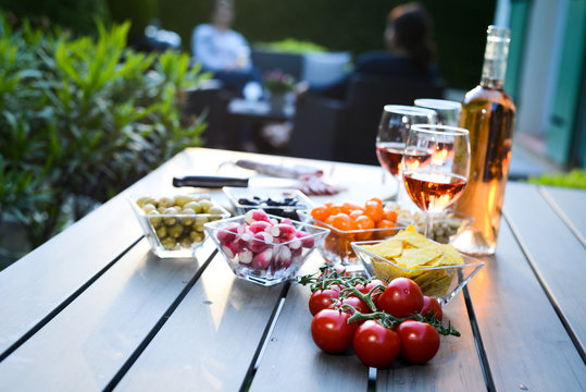 holiday summer brunch party table outdoor in a house backyard with appetizer, glass of rosé wine, fresh drink and organic vegetables