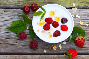 Homemade yogurt with raspberries, strawberries and sour cherries, with grain cereals flakes on a wooden table