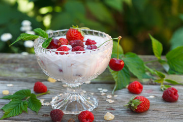 Homemade breakfast with yogurt, corn flakes, oatmeal, raspberries and other cherries in glass bowl on rustic wooden table