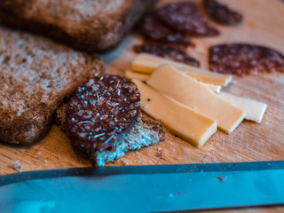 Sliced salami with seasoning, cheese and toasts on a wooden table with a knife in foreground