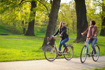 Obraz premium Two young women ride bikes in the spring park.